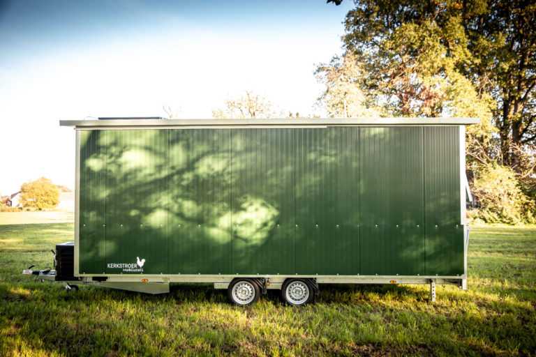 Ein mobiler Hühnerstall in grün mit zwei Rädern, der auf einer Wiese steht.
