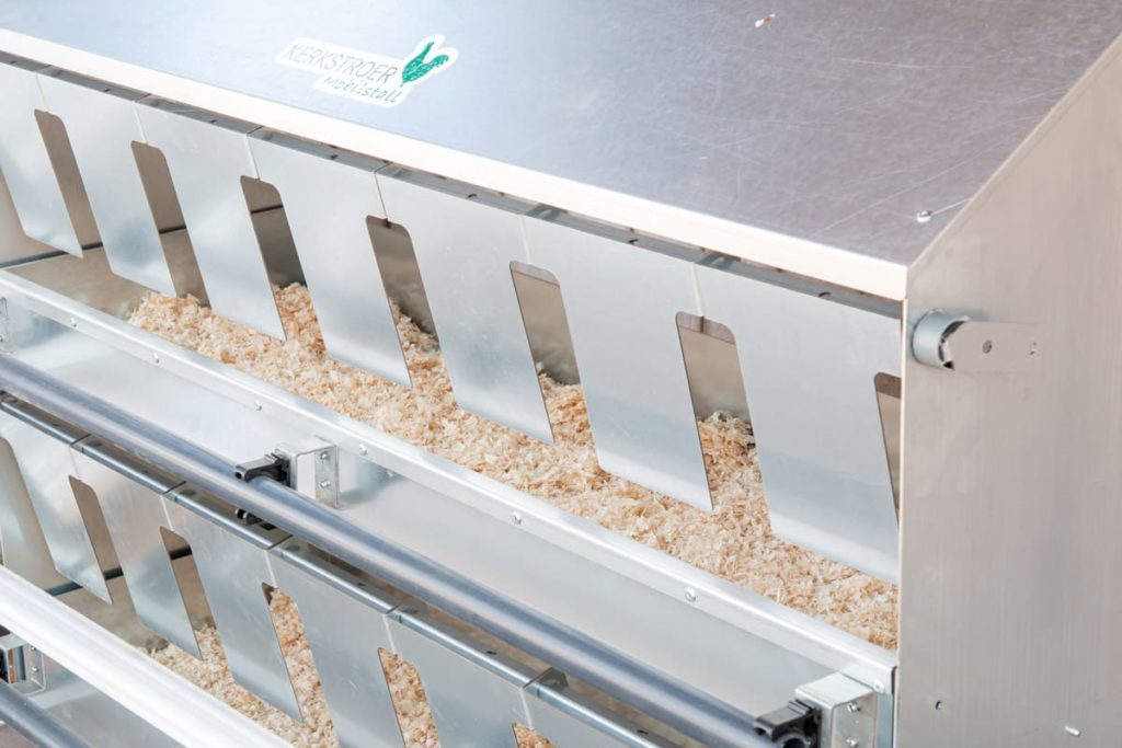 Ein mobiler Hühnerstall mit silberner, metallischer Futterstation, die mit Sägespänen gefüllt ist.