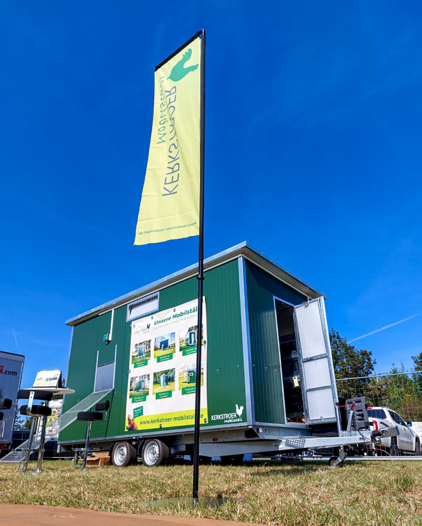 Ein mobiler Hühnerstall von Kerkstroer Mobilstall auf einem Messestand, mit einer grünen Außenfarbe und einem Werbebanner.