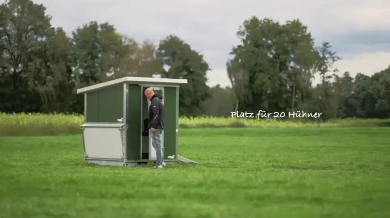 Ein Mann steht vor einem Hühnerstall auf einer Wiese, der Platz für 20 Hühner bietet.